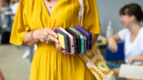 Getty Women in yellow dress holding multiple cell phones